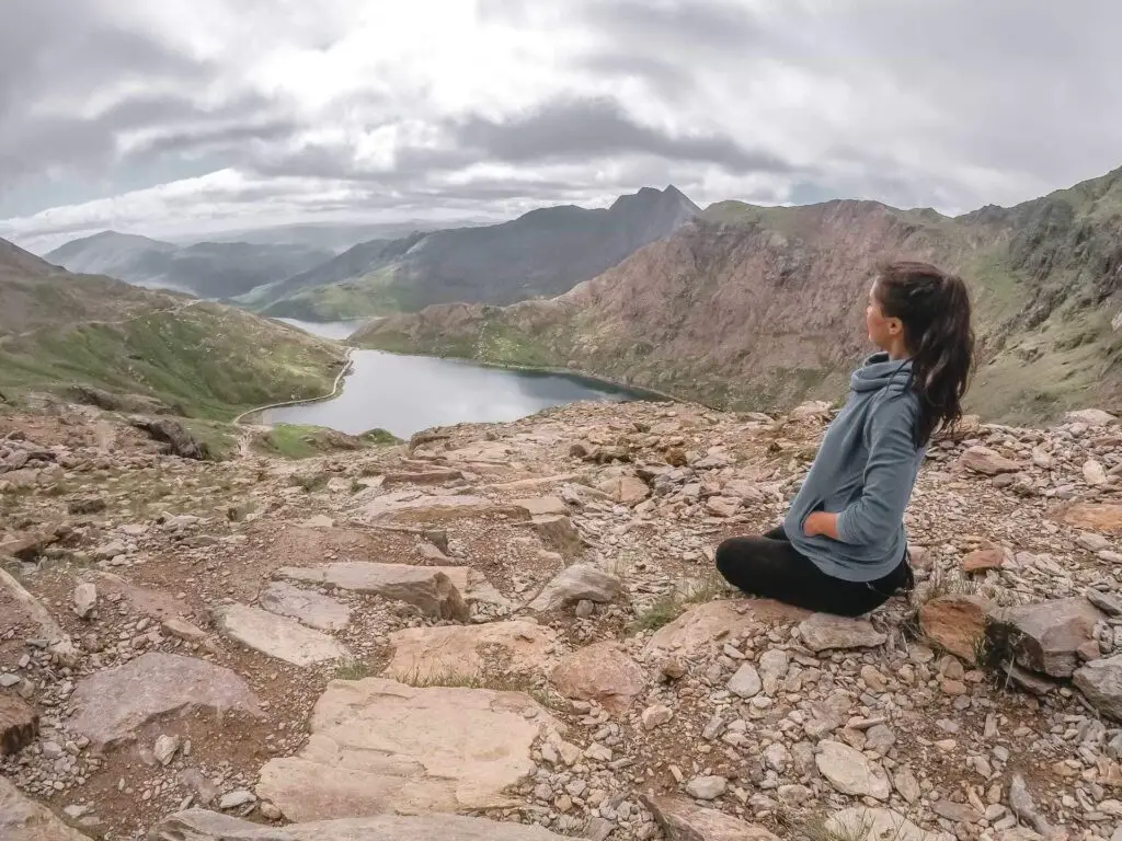 Zoe sitting down with hip pain from her injury. She is on mount Snowden looking down into the valley,
