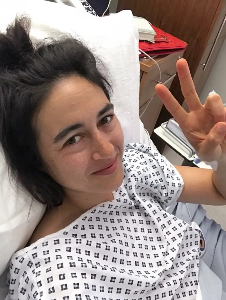Zoe tehrani in a hospital gown taking a selfie post op