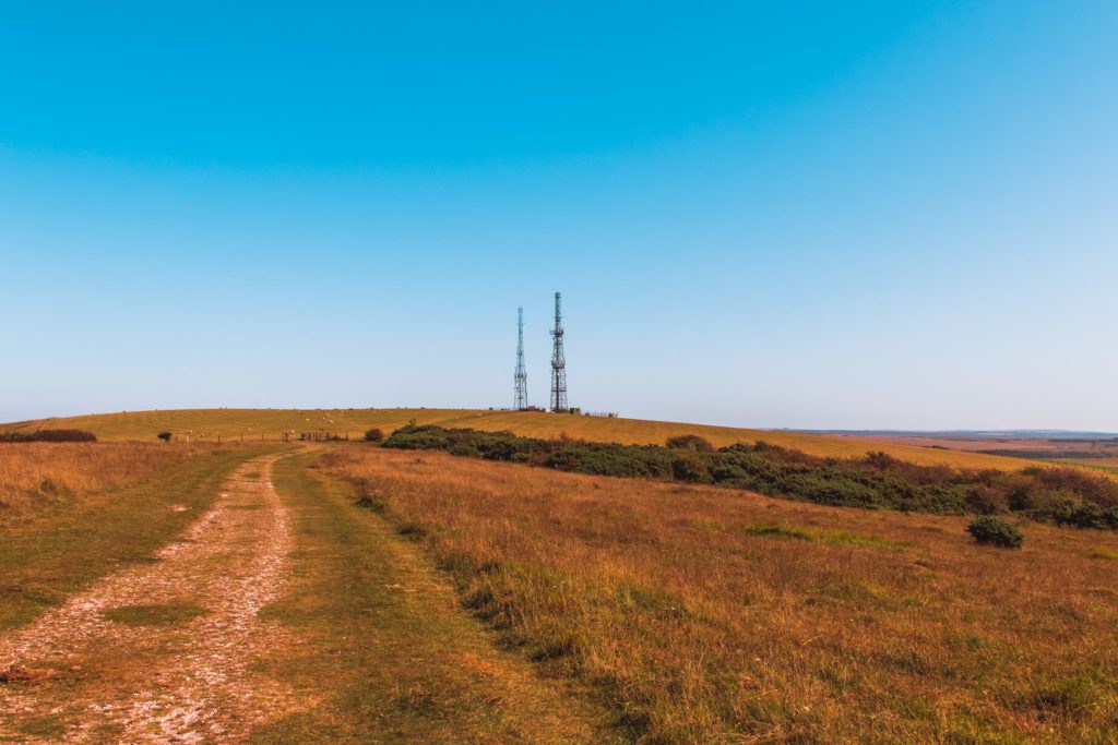 The South Downs Way path running through a field with a view of two telephone pylons in the distance, with a blue sky backdrop. 