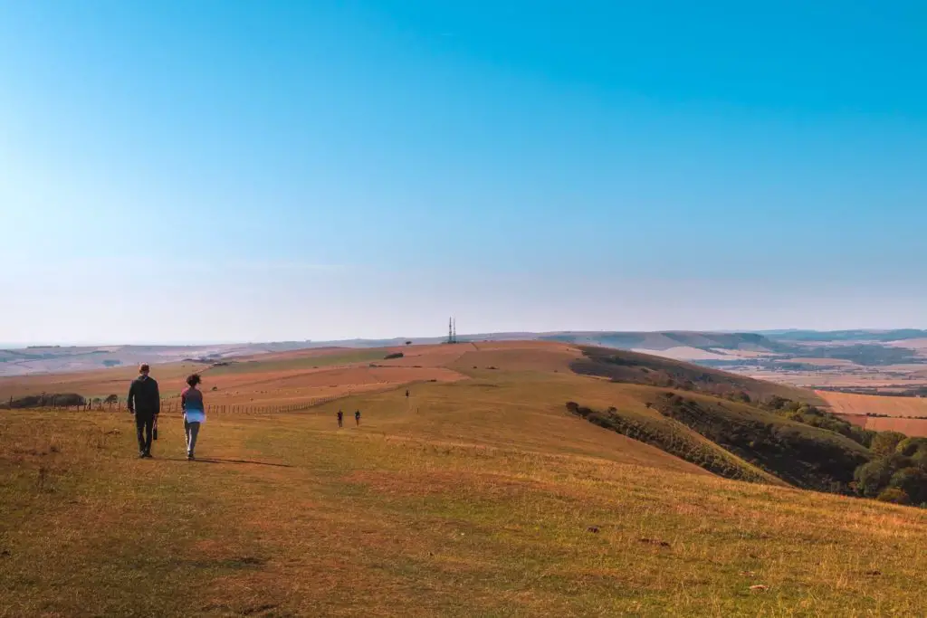 A hill top view of the South Downs, with people walking along the top.