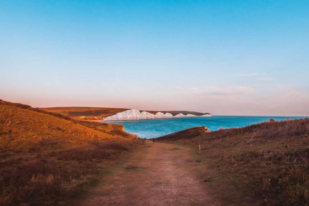 Looking along the walking trail near Seaford, towards the white chalk cliff of the Seven Sisters in the distance. The sea under it is bright blue.