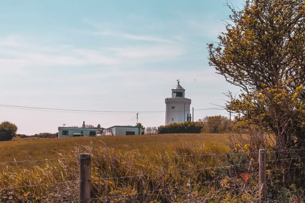 South Foreland lighthouse on a sunny day. It is half hidden behind bushes on the other side of a green field. 