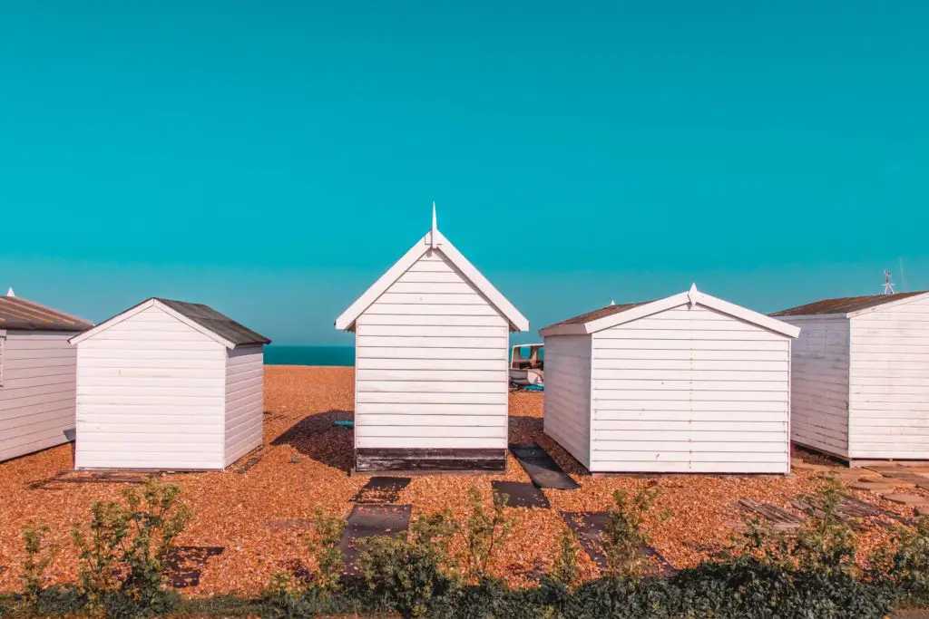 Beach huts on a shingle beach with a backdrop of bright blue sky near the end of the walk from Dover to Deal.  