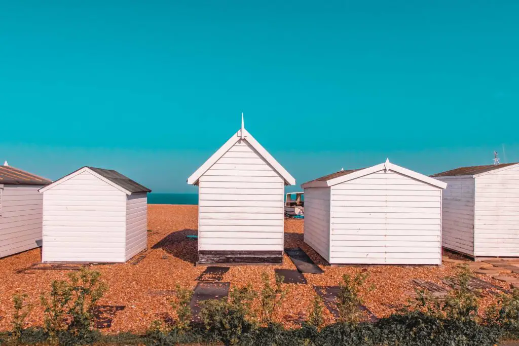 Beach huts on a shingle beach with a backdrop of bright blue sky near the end of the walk from Dover to Deal. 