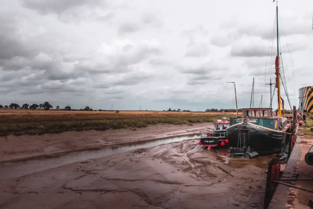 A boat resting on the river bed whilst the tide is out, on a cloudy day.