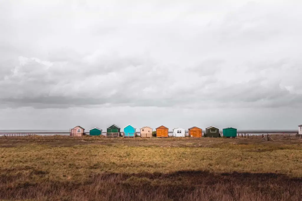 A row of colourful shabby beach huts on the other side of the field, on one of the coastal walks from London.