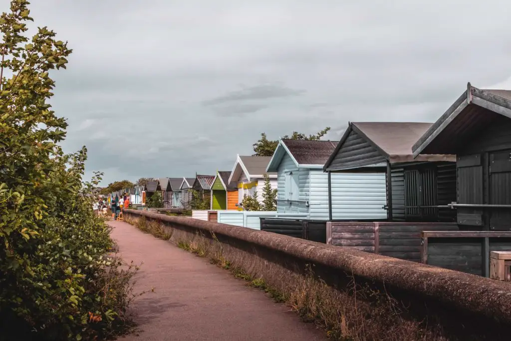 A row of colourful beach huts behind a sea wall, approaching Whitstable.