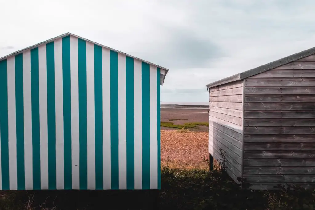 A blue and white stripped beach hut next to a plain wooden beach hut.
