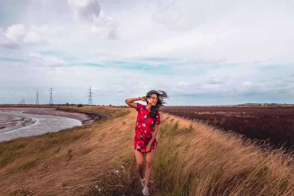 Zoe wearing a red dress with hair blowing in the wind walking along the trail from Faversham to Whitstable. 