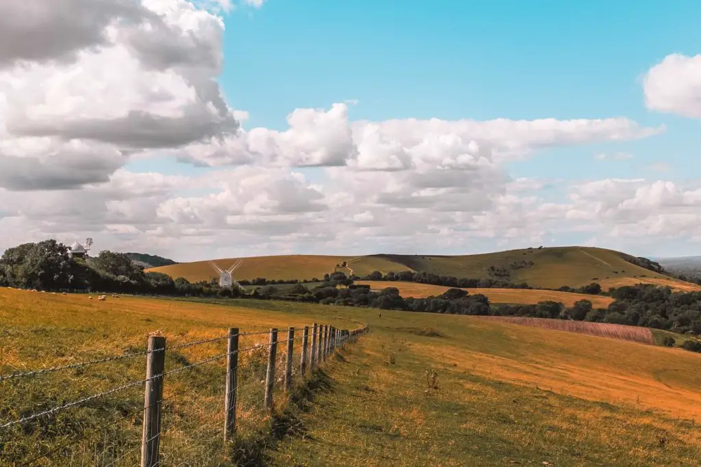 A field with the rolling hills in the distance. The Jack and Jill Windmills are in the left of the frame. There is a fence separating this field and the one to the left. 