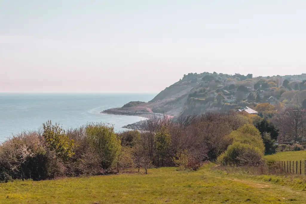 A view looking back at a village on a hill next to the ocean on the Hastings to Rye coastal walk.