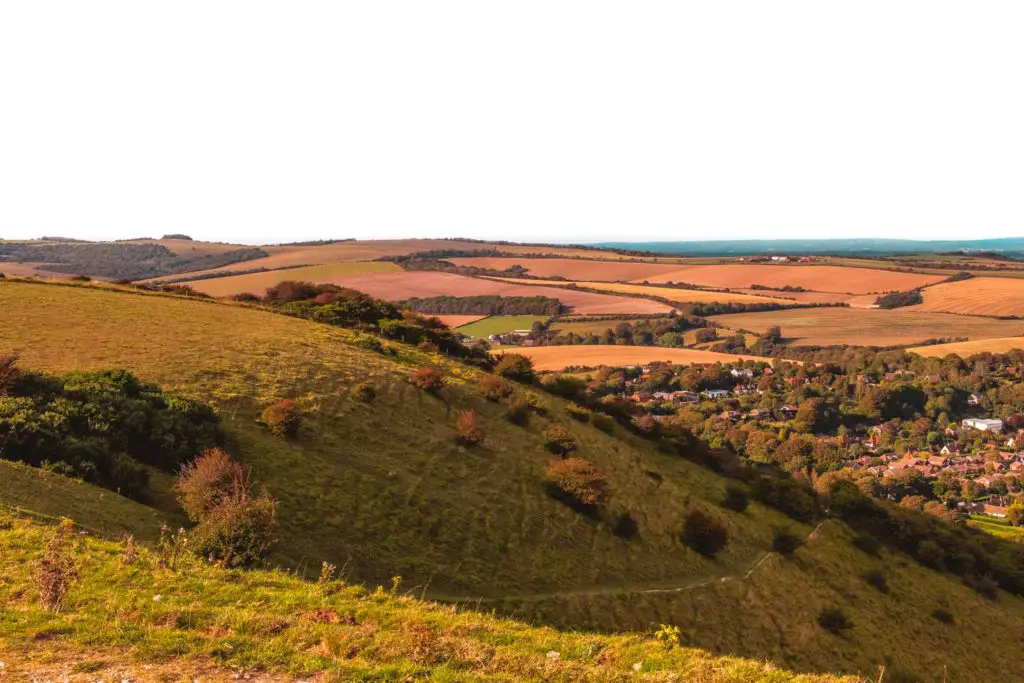 A green grass hill with a steep incline and a view of a village and lots of trees below on the walk from Lewes to Southease.