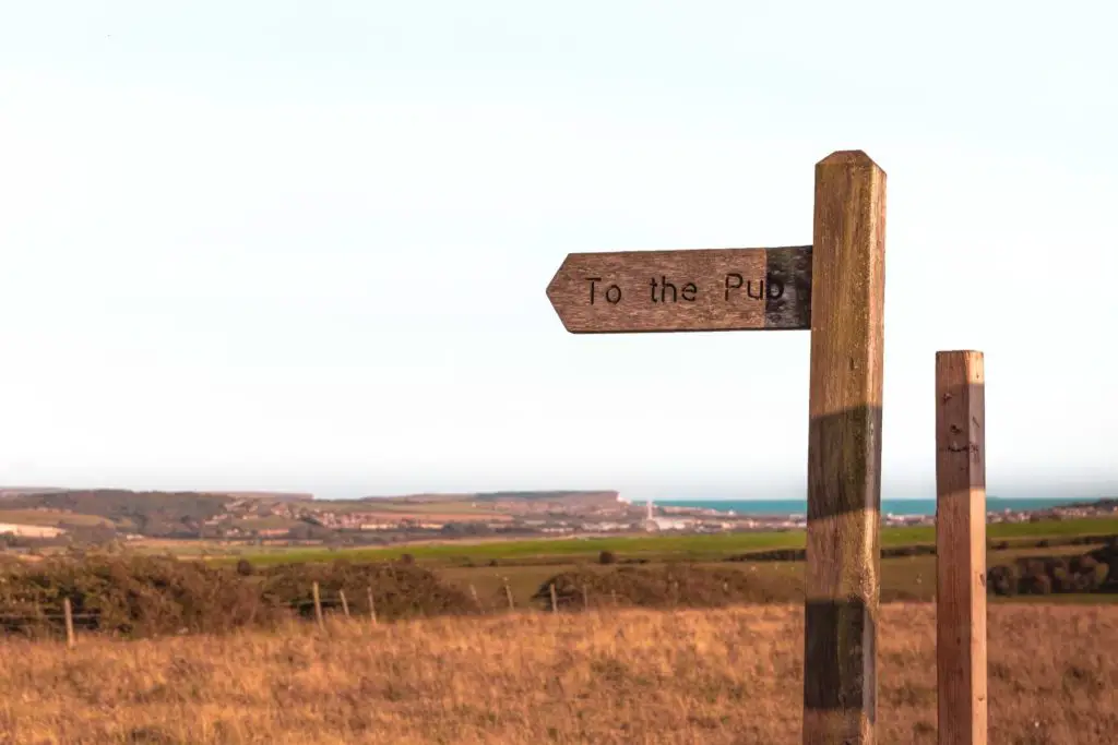 Signage pointing to the pub with fields and ocean view in the background. 