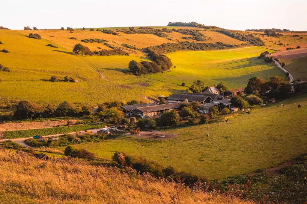 A farm house in a valley of the green and orange coloured hills with trees dotted around.