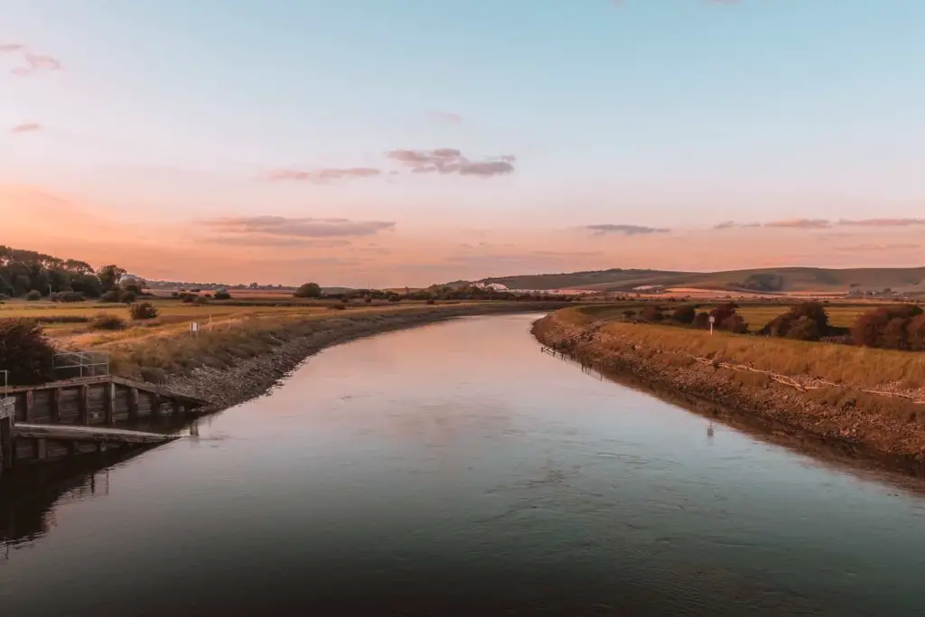 The river Ore leading from the bottom of the frame into the distance as it curves to the right. The river is still and calm, and there is a warm hue as the sun is setting.