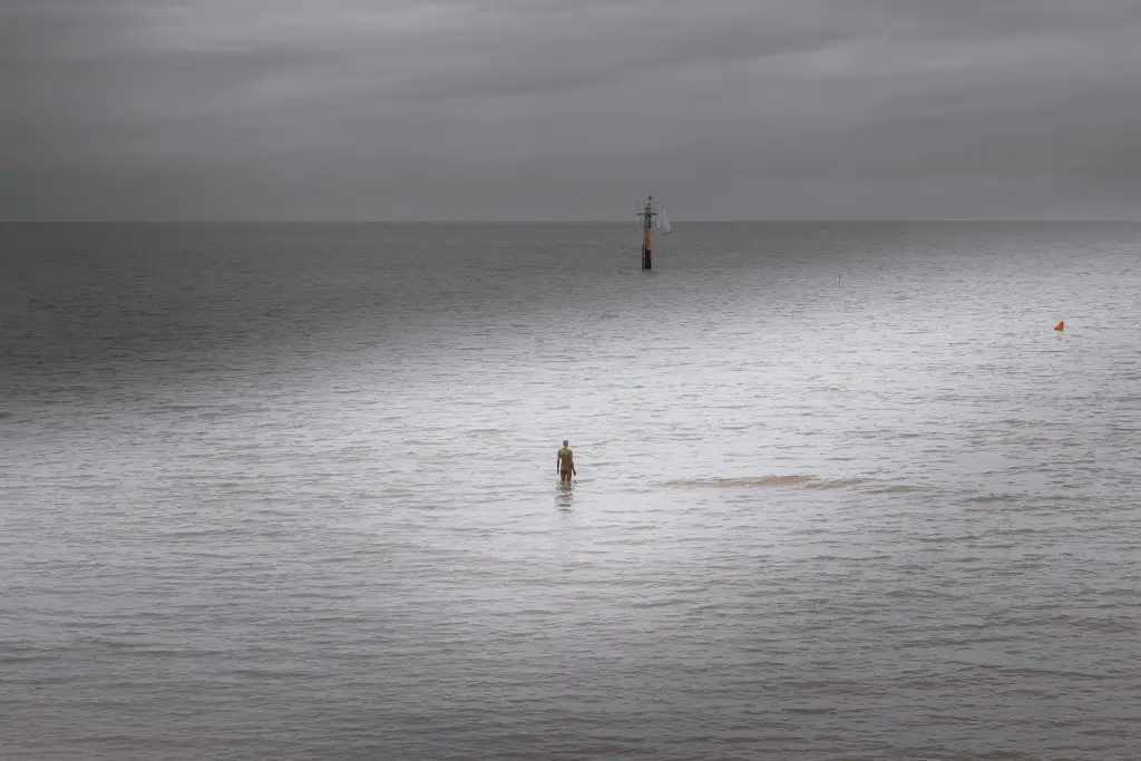 The cloud covered grey sky and sea with an iron man sculpture in the water in Margate.