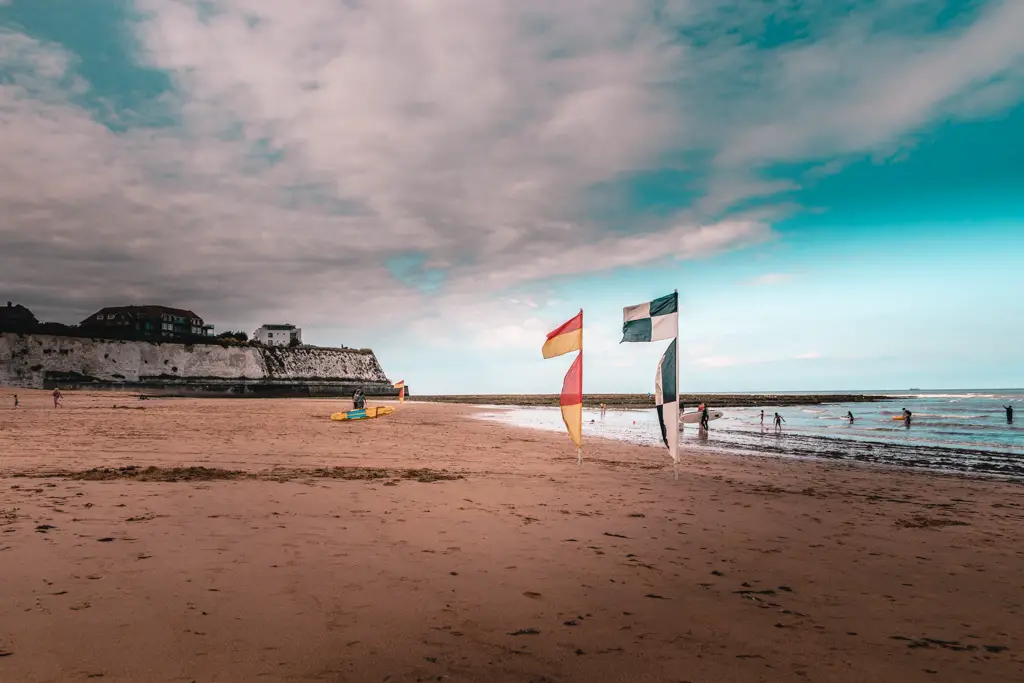 A beach cove with flags and surfers coming out of the water. The sky is clearing up.