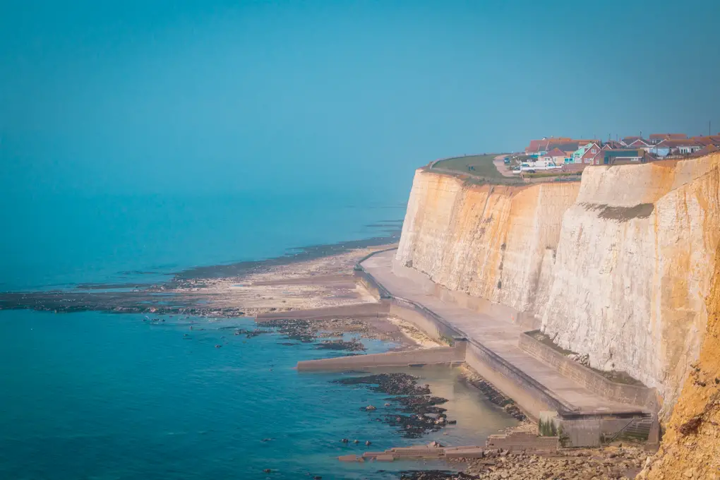 The large white cliffs with an under cliff walkway on one of the coastal walks near London. There are houses on top of the cliff. the sea and sky is blue.