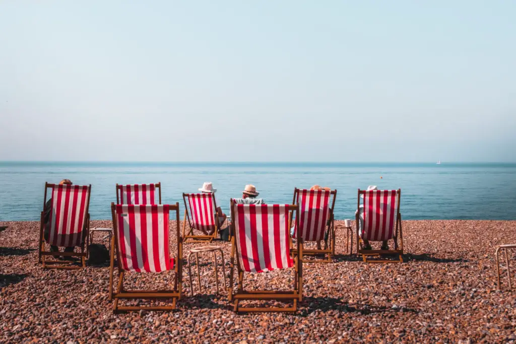 8 red and white stripped deckchairs on the shingle beach at Seaford. There are two men sitting on the chairs looking out to the blue sea.