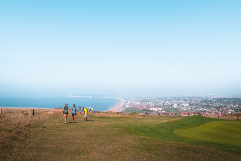 A hill top view over the town of Seaford, on the walk to Eastbourne. It meets a strip of beach and then the blue ocean and blue sky. 