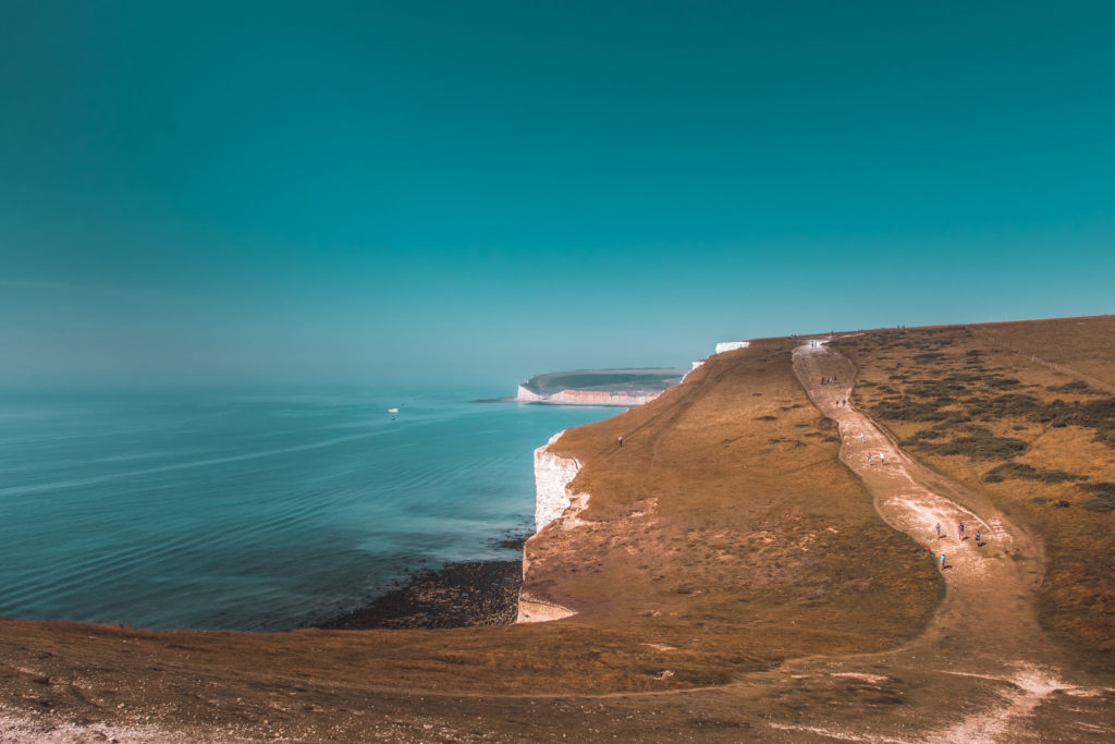 A view of the Seven Sisters hike trail on the green grass clifftop. The sea to the left is blue.