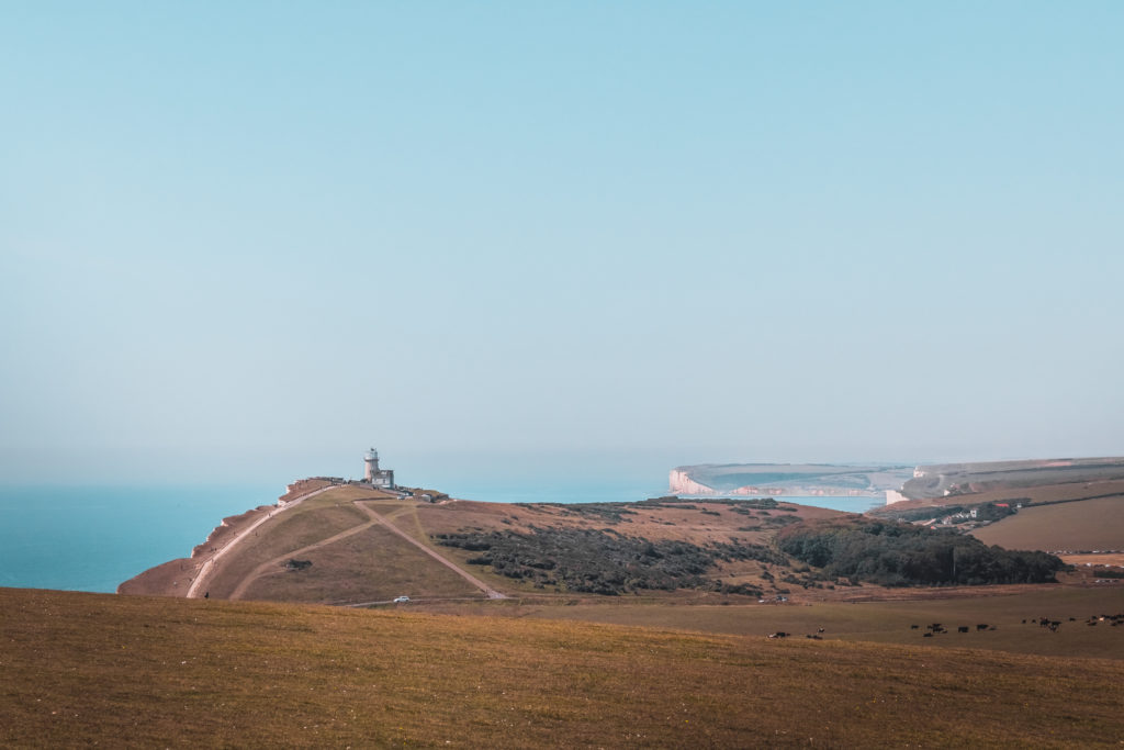 A view of the green clifftop landscape with Belle Tout lighthouse in the distance on the Seven Sisters hike.