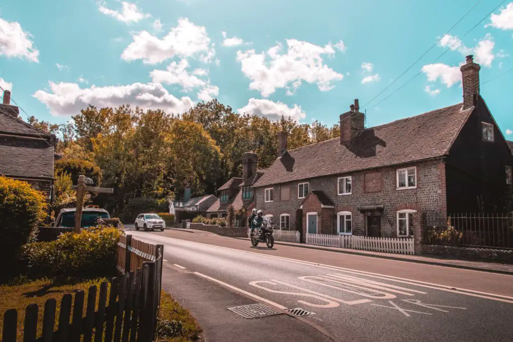 A road with a house on the other side and a motorcyclist riding along the road.