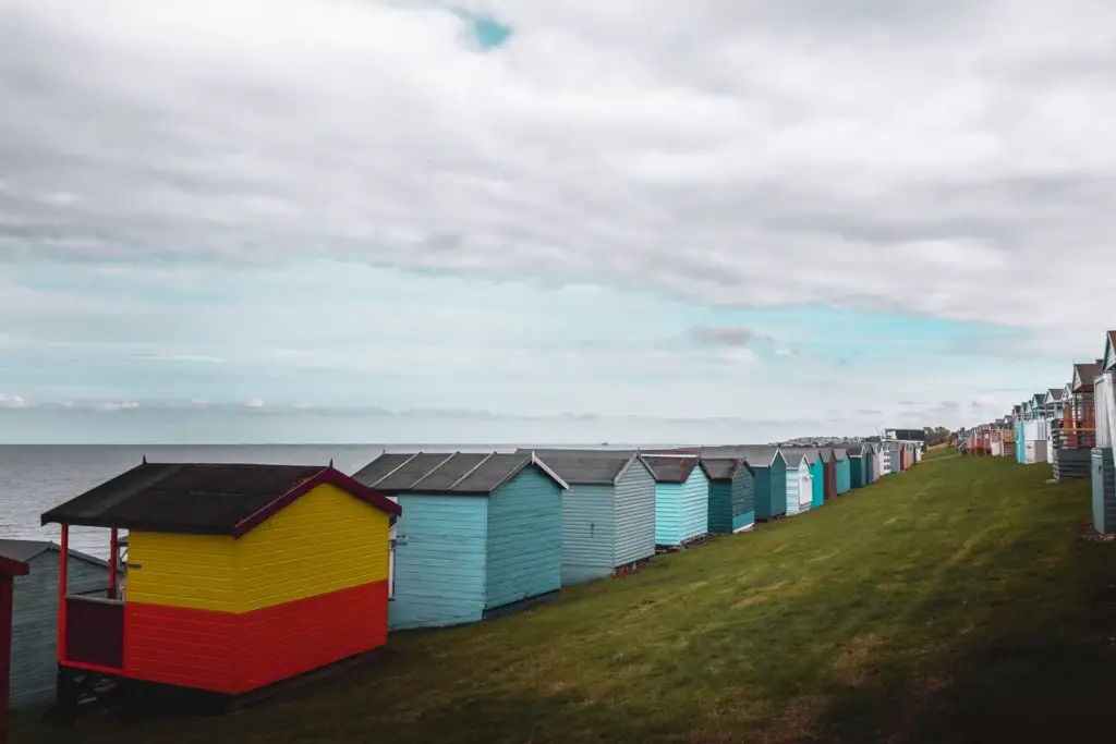 Standing between rows of beach huts on a green hill with the sea in front.