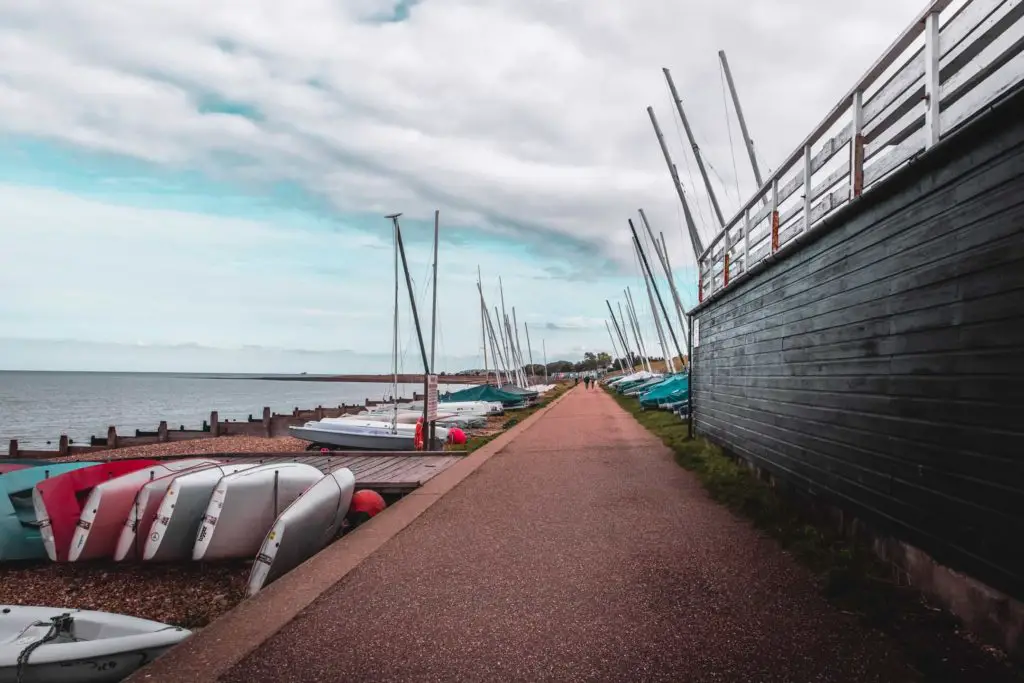 The coastal trail on the walk from Whitstable to Herne Bay. There is a black wooden wall on the right of the frame, and mini yachts on the shingle on the left.