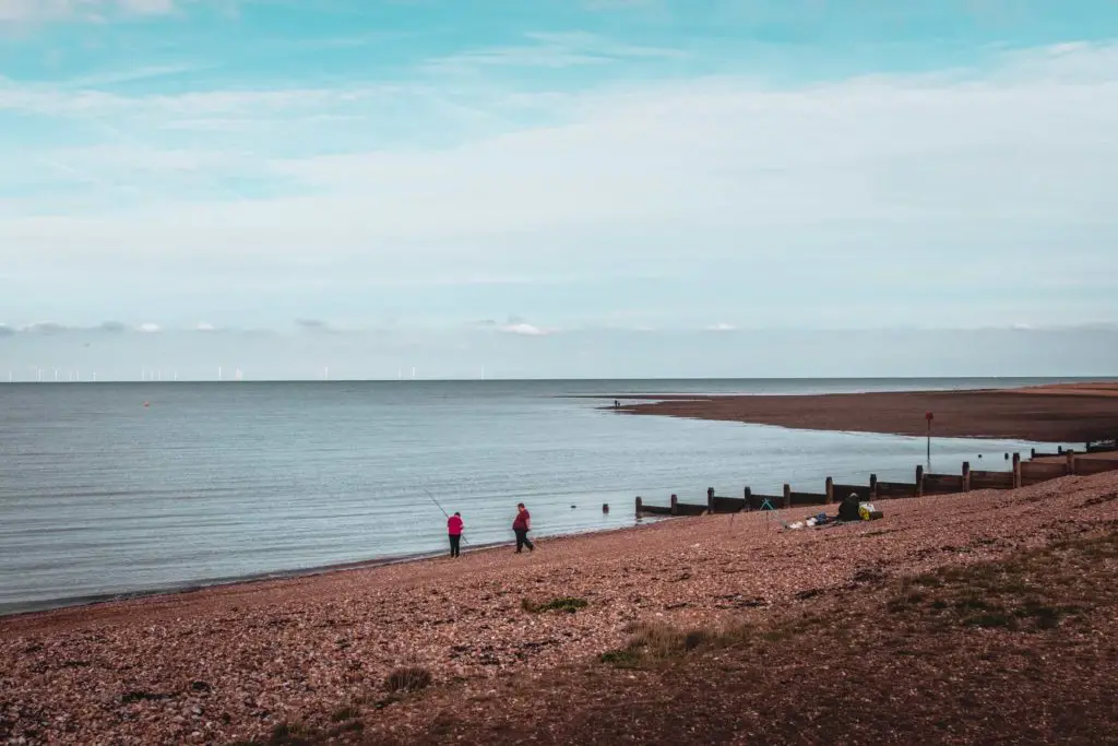 The shingle beach meeting the dark coloured sea. There are two people fishing.