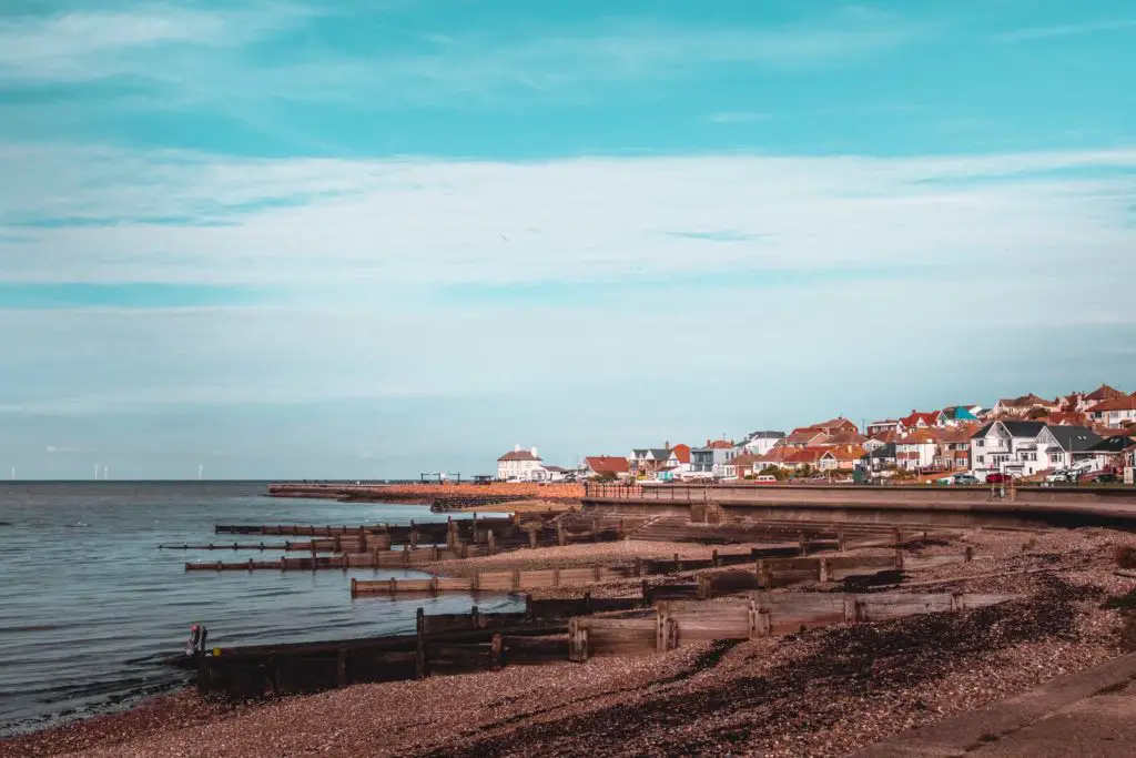 A view of a group of buildings of Whitstable where they meet the sea. The sky is blue with white cloud streaks.