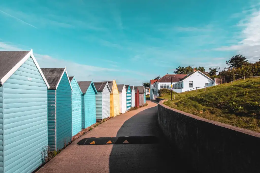 A curved path on the coastal walk from Whitstable to Herne Bay. The left side of the path is lined with colourful beach huts, the right side is enclosed by a wall.