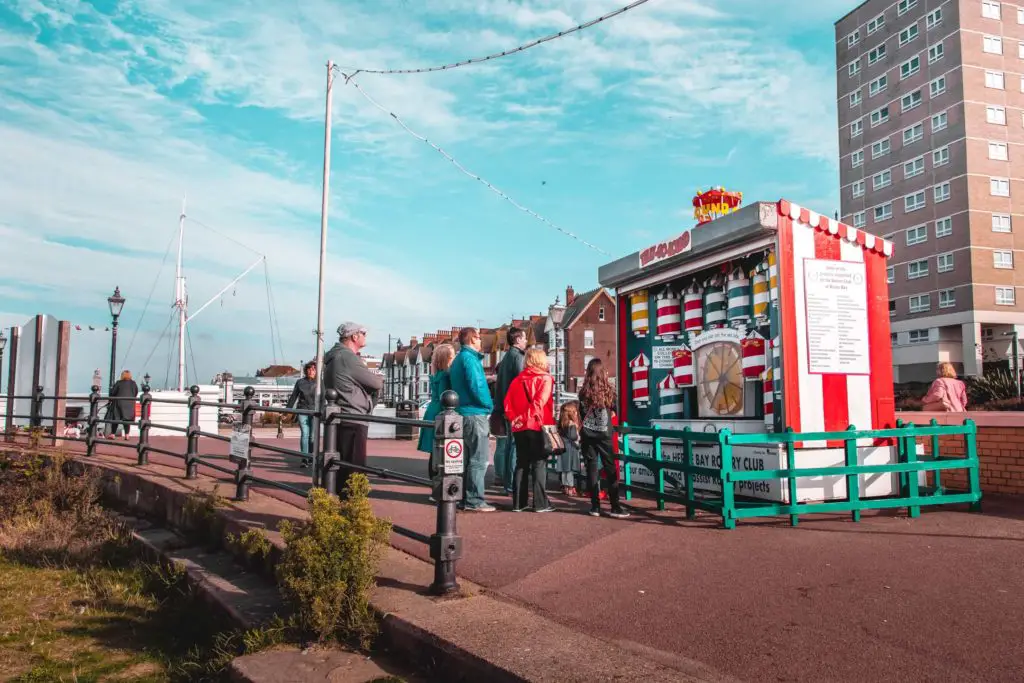 A group of people standing in Herne Bay, looking at a fair ground amusement game.