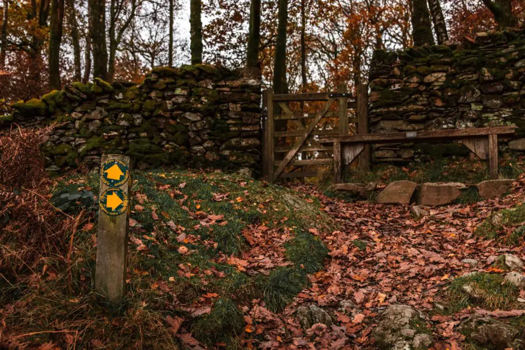 A wooden stump with trail directions standing in front of a stone wall with a wooden gate.