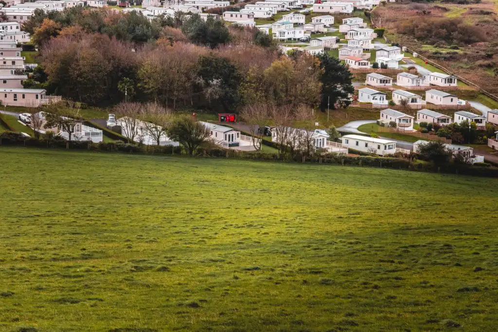 A cluster of white holiday park homes on the other side of an empty green field.