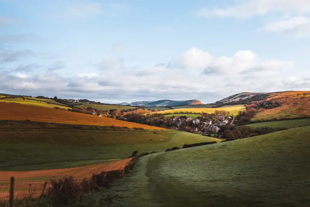 A view down into the valley and a cluster of houses on the walk from Lulworth Cove to Durdle Door. The rolling hills are shades of green and orange.