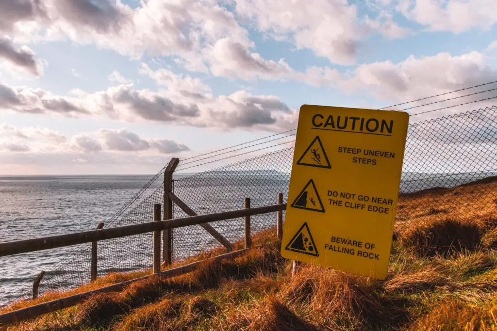 Yellow signage warning of danger of falling near the cliff edge on the Lulworth Cove hike.