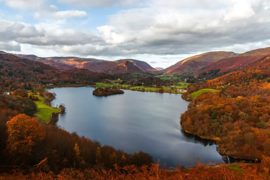 A view down to Grasmere surrounded by trees in different shades of orange and mountains in there background in the Lake District.
