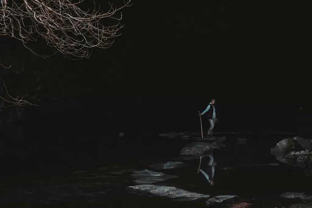 A women standing on a walking stone in a blacked out cave.