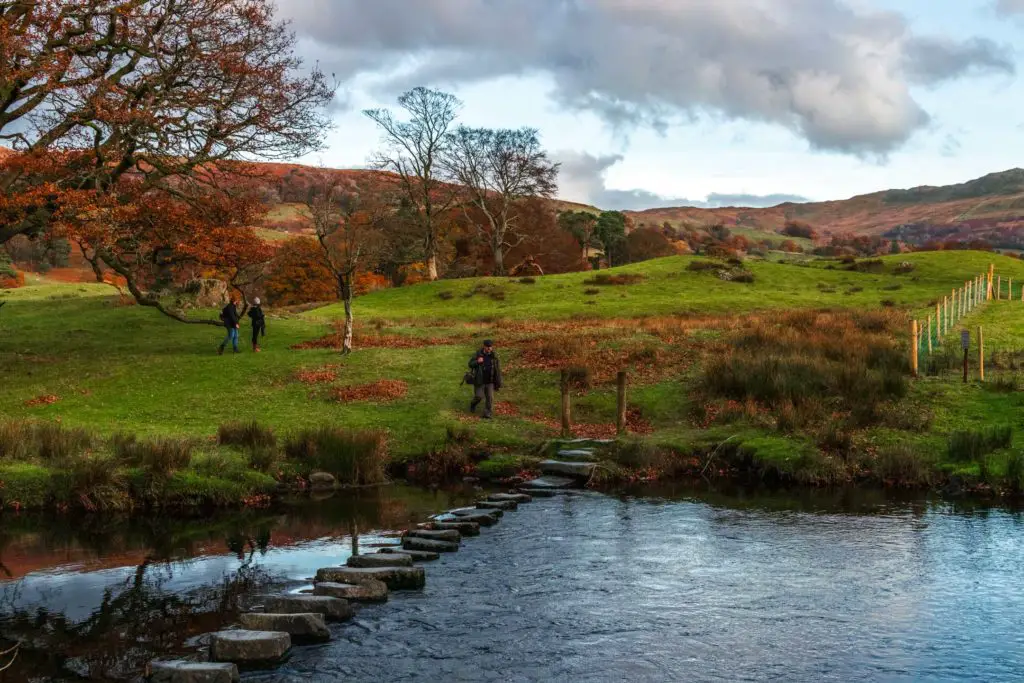 Steeping stones over the water with a green field on the other side on the walk towards Ambleside. There is a man on the other side walking to the stepping stones.