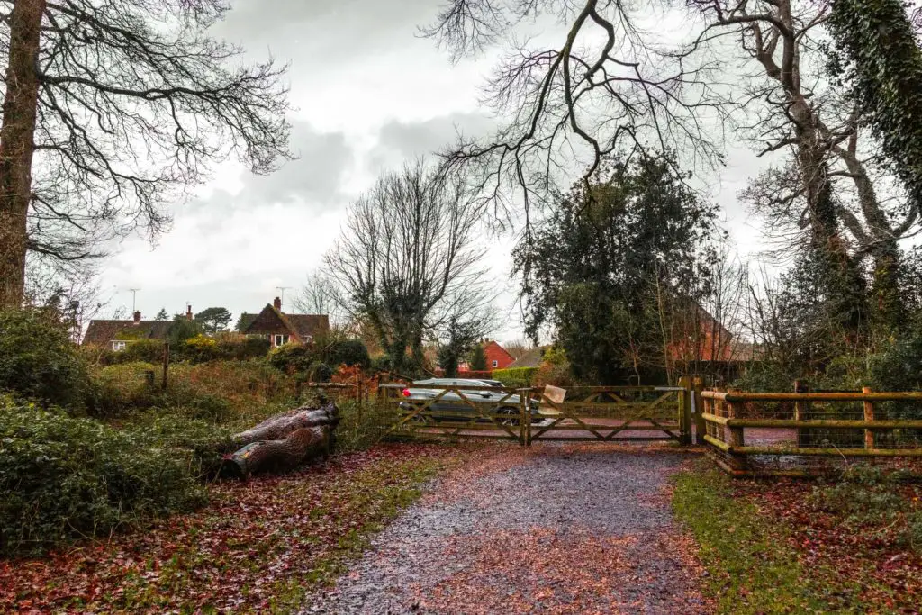 A path leading to a wooden gate with a car and houses on the other side. 