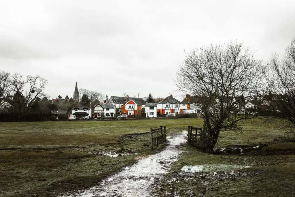 White and orange coloured houses not the other side of the green field at the end of the walk from Ashurst to Lyndhurst in the New Forest. It is an overcast day.