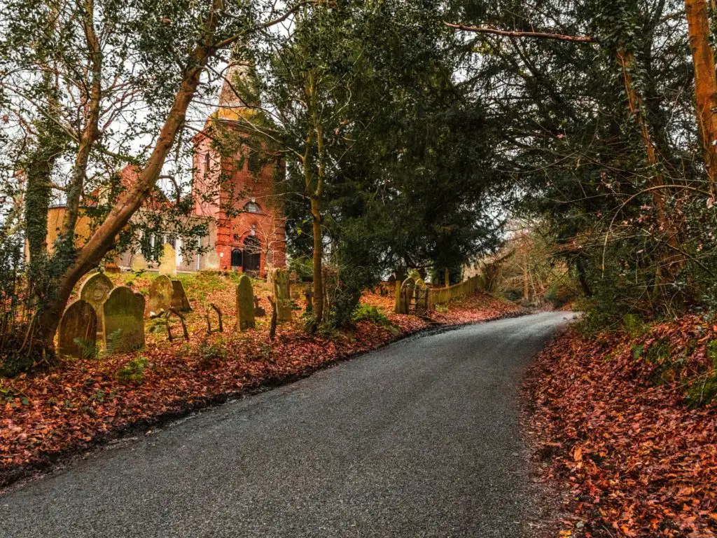 The tarmac road running uphill next to a church and graveyard on the left at the start of the walk from Brockenhurst to Lymington.