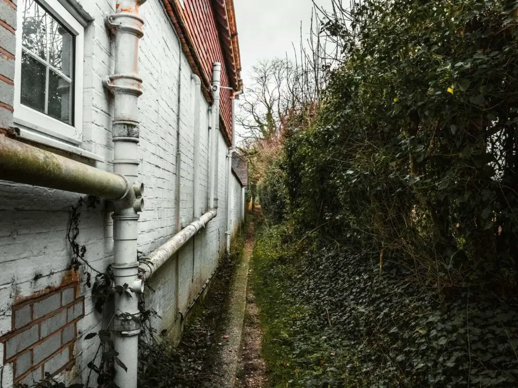 The trial leading down the back of houses. Houses on the left and bushes on the right.