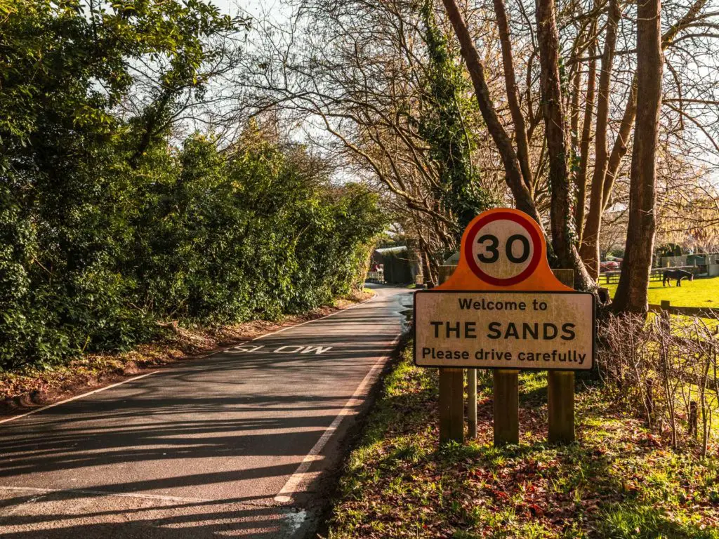 The main road with a big green hedge on the left and a sign welcoming you to the sands on the right.