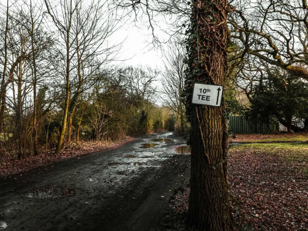 A white sign stuck on a tree pointing to the 10th tee. 