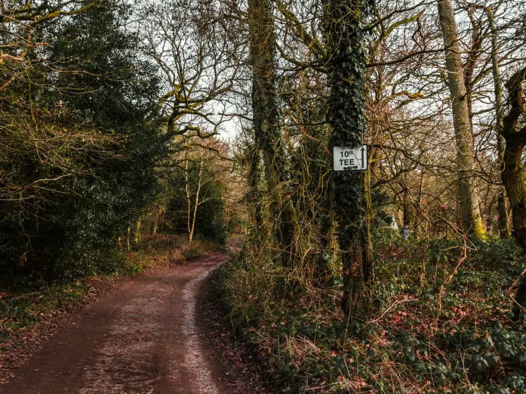 the dirt trail running alongside a white sign stuck on a tree pointing to the 10th tee. 