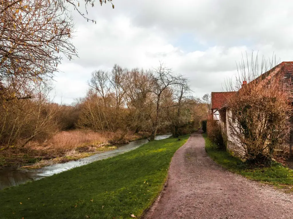 A trail running along side a house on the right with a strip of green and river to the left.