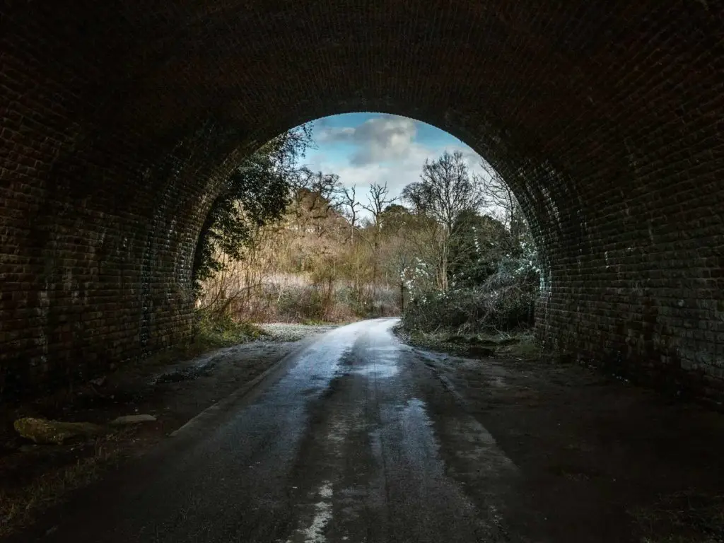 Walking through a tunnel with a view to trees and bushes and a blue sky through the tunnel.