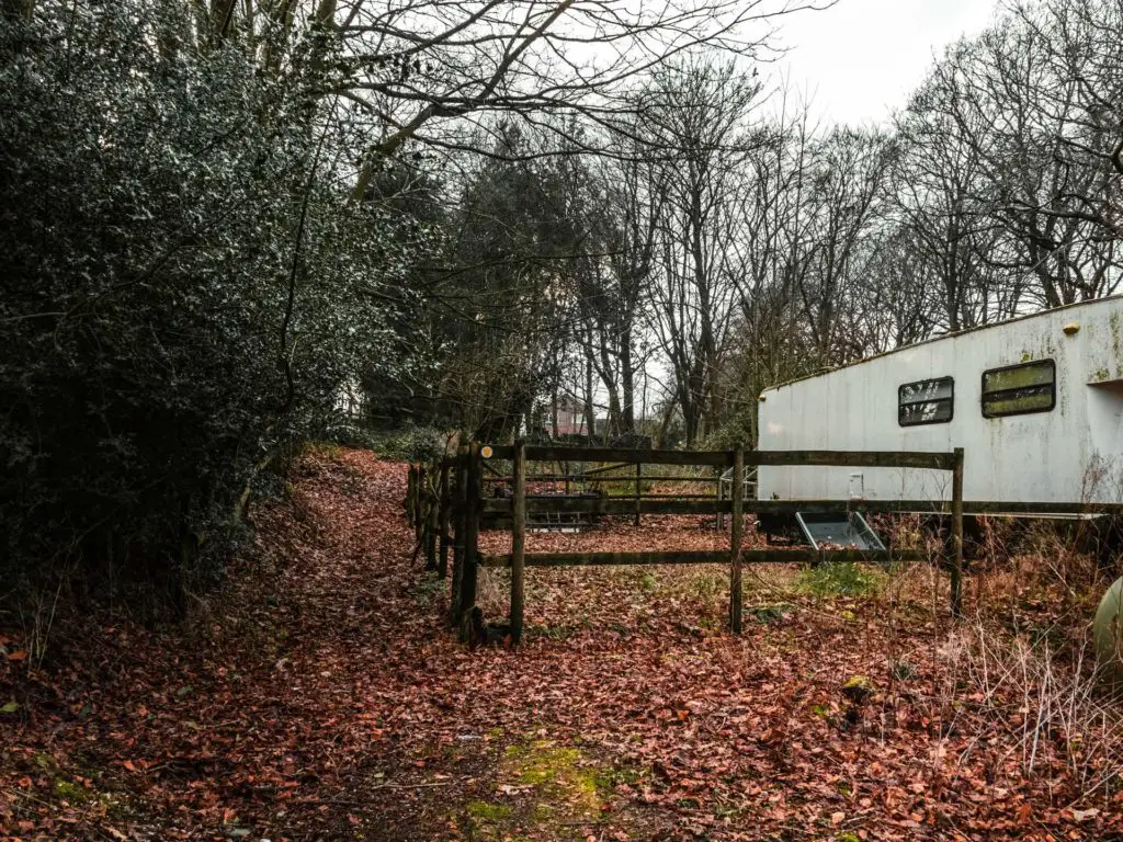 A leaf covered ground with a fence and a white caravan on the right.